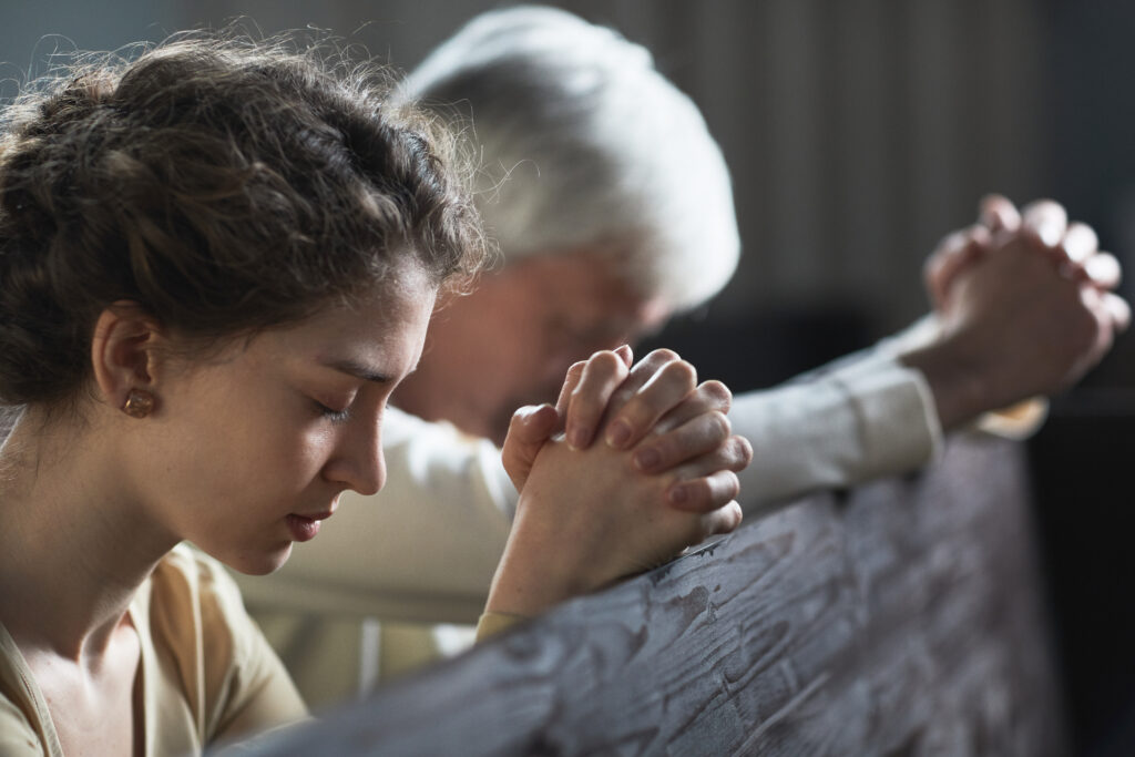 Two people praying with clasped hands inside a church during a quiet moment of reflection
