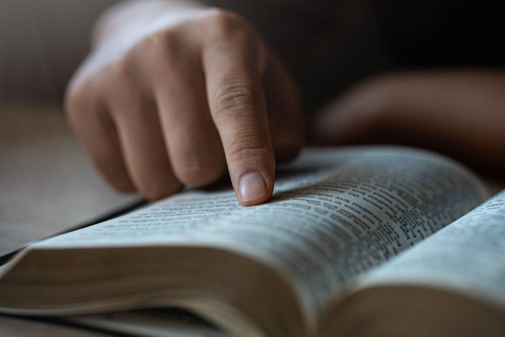 A hand pointing to a verse while reading an open Bible in a quiet, reflective setting