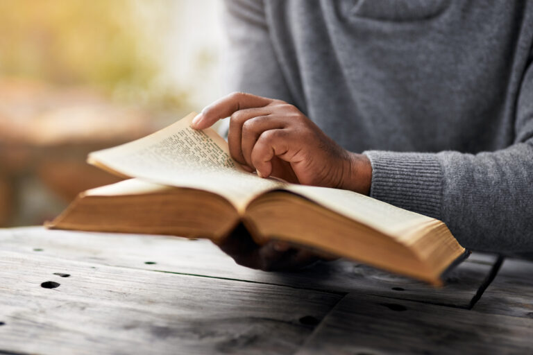 A person reading an open book while pointing to a line of text in a calm, focused setting